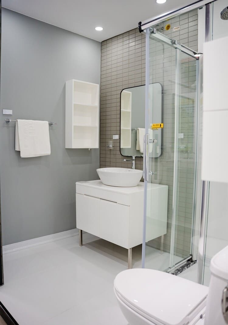 Phòng tắm hiện đại với bồn rửa mặt trắng và gương lớn cạnh phòng tắm kính, thiết kế tối giản và tinh tế.