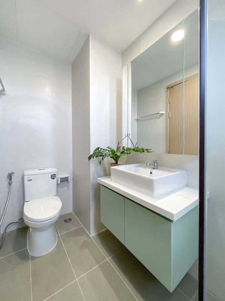 Phòng tắm hiện đại với bồn rửa, gương lớn, cây xanh, và bồn cầu, thiết kế tối giản.