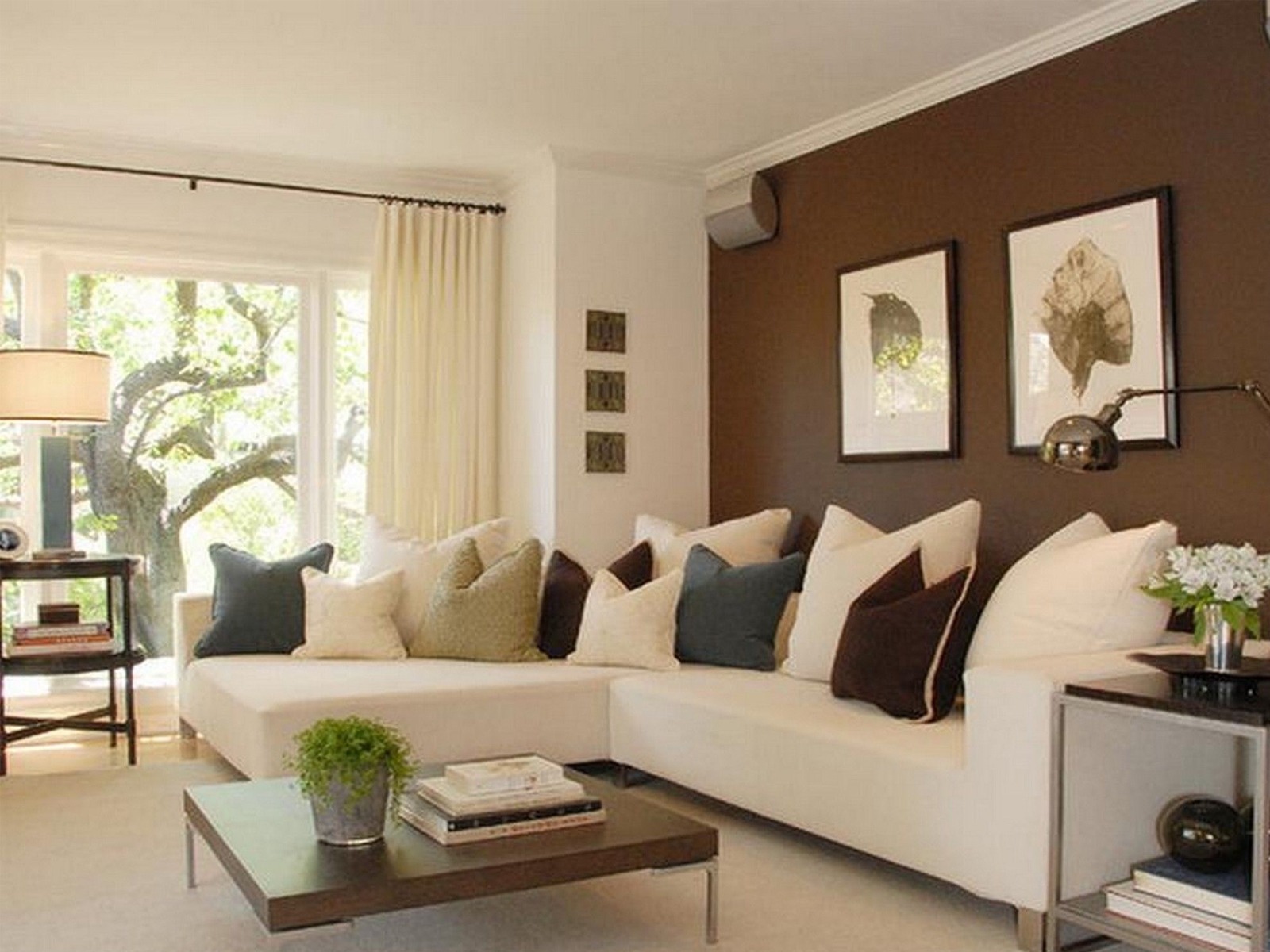 Phòng khách hiện đại với ghế sofa trắng, gối ôm và tranh treo tường, ánh sáng tự nhiên qua cửa sổ lớn.