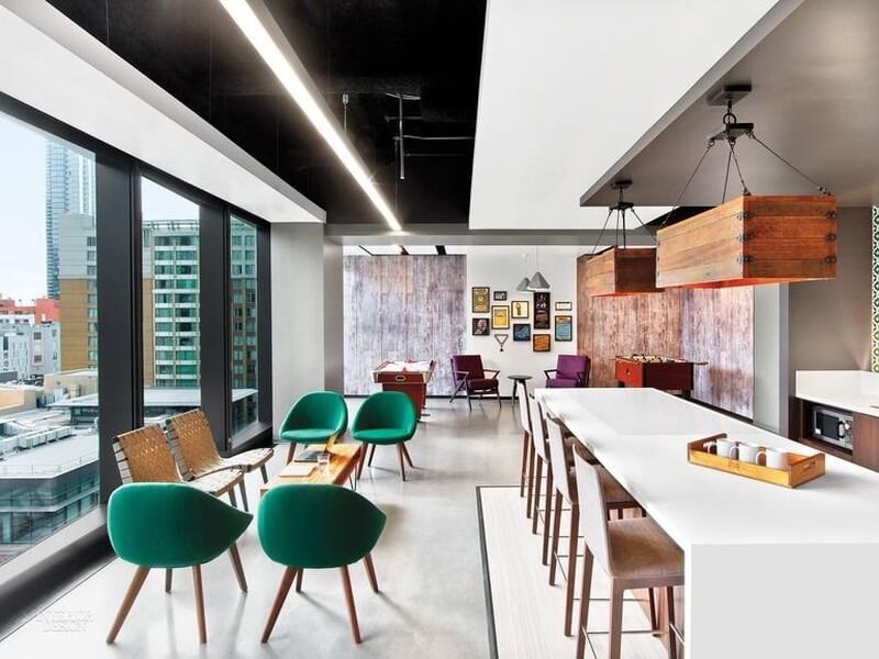 Không gian văn phòng hiện đại với ghế xanh, bàn dài, cửa sổ lớn nhìn ra thành phố.