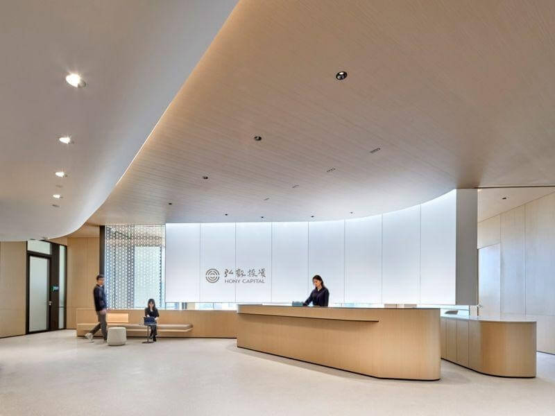 Sảnh tiếp tân hiện đại với quầy lễ tân và người làm việc, không gian sáng và nội thất gỗ.