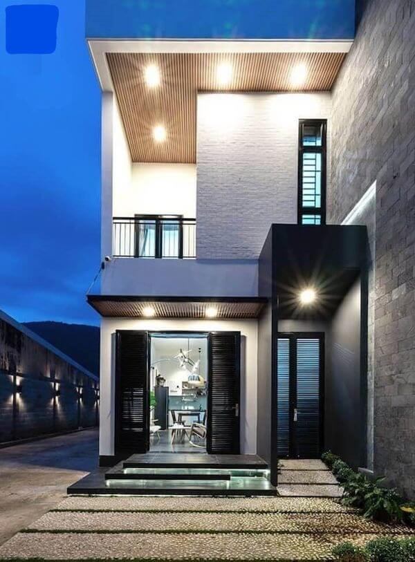 Ngôi nhà hiện đại hai tầng với ánh đèn sáng vào buổi tối, thiết kế kiến trúc độc đáo và cửa sổ lớn.