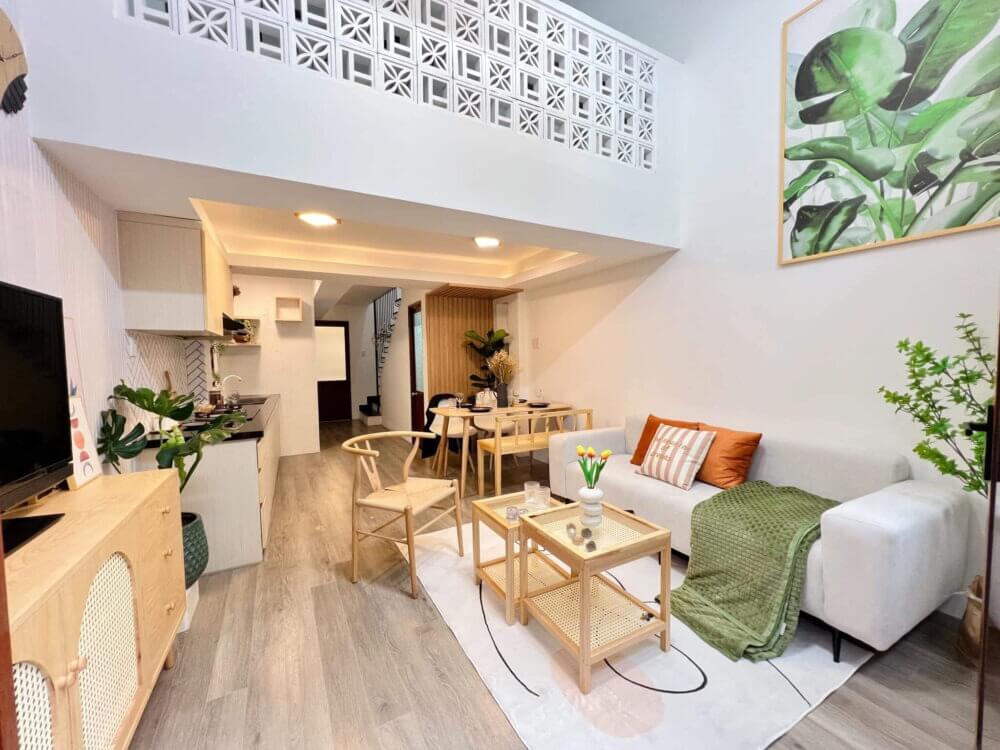 Phòng khách hiện đại với nội thất gỗ, sofa trắng, trang trí cây xanh và tranh treo tường lá cây xanh.