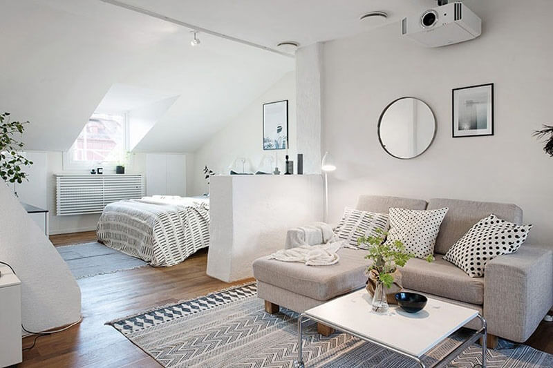 Phòng khách hiện đại với sofa xám, bàn trà trắng, giường ngủ và cửa sổ mái, không gian sáng tạo và thoáng đãng.