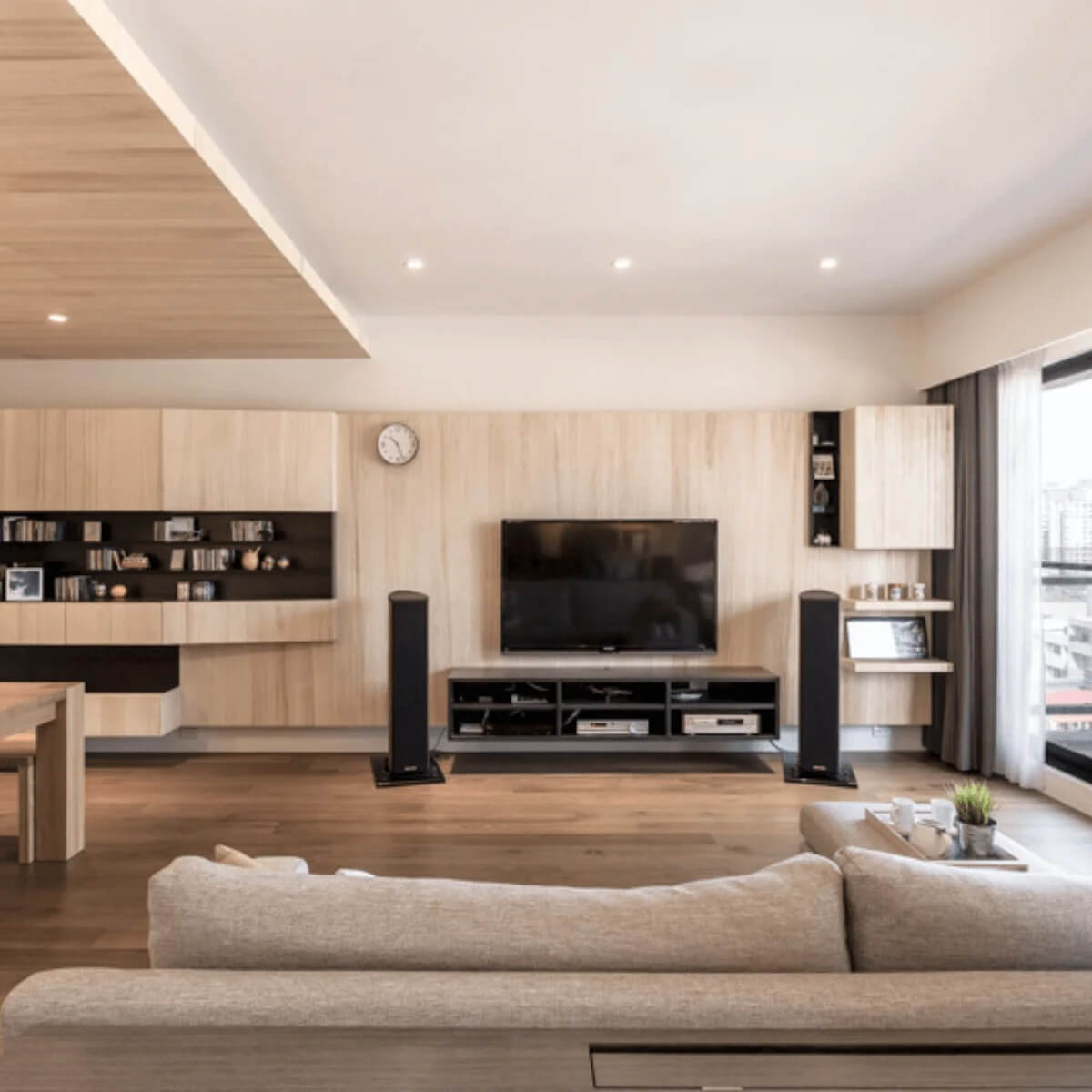 Phòng khách hiện đại với nội thất gỗ, TV màn hình phẳng, và ghế sofa màu be.