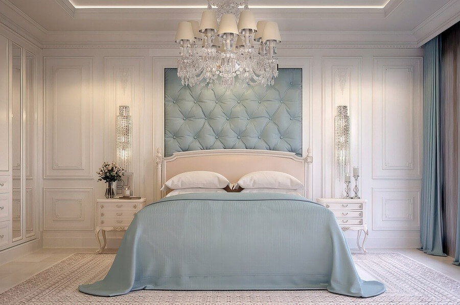 Phòng ngủ sang trọng với giường lớn, đèn chùm tinh xảo và tường màu xanh dương nhạt.