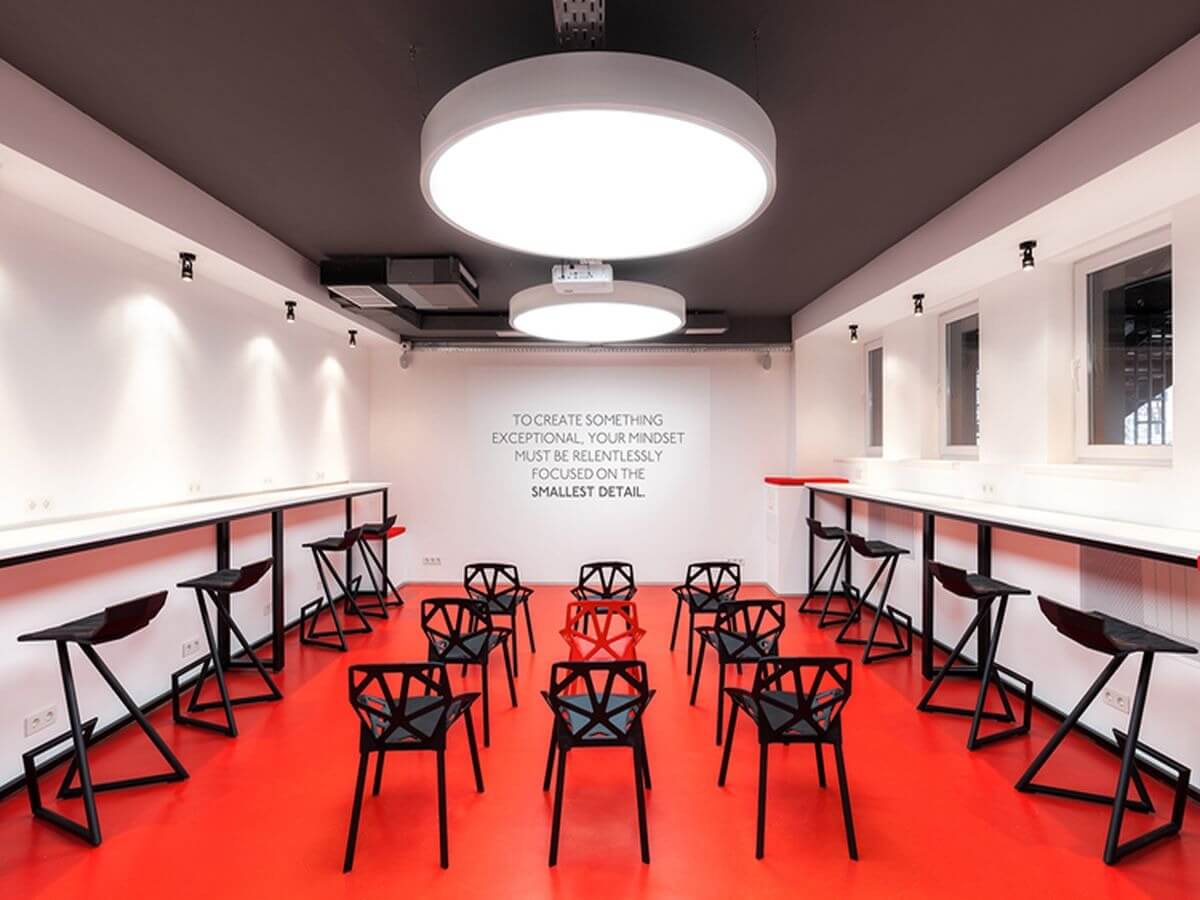 Phòng họp hiện đại với sàn đỏ, ghế đen và ánh sáng trắng, có câu triết lý trên tường.