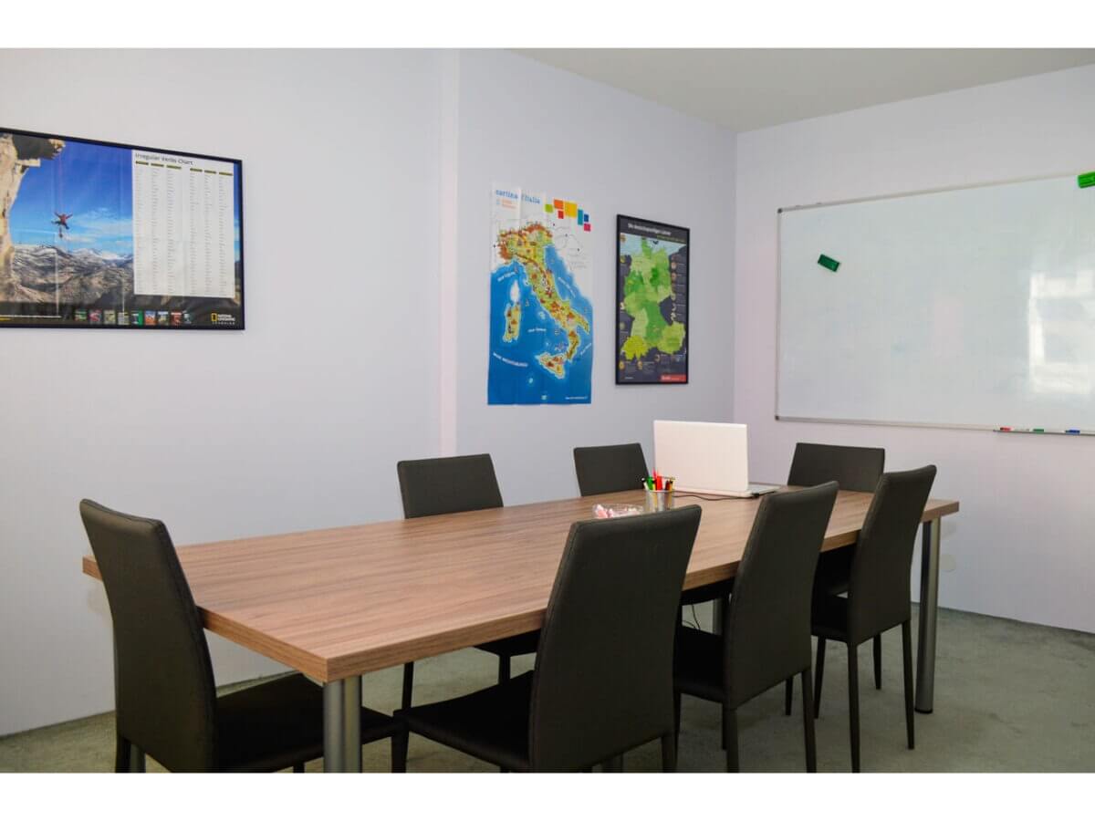 Phòng họp với bàn gỗ, ghế đen, laptop và bảng trắng, trang trí bản đồ trên tường.