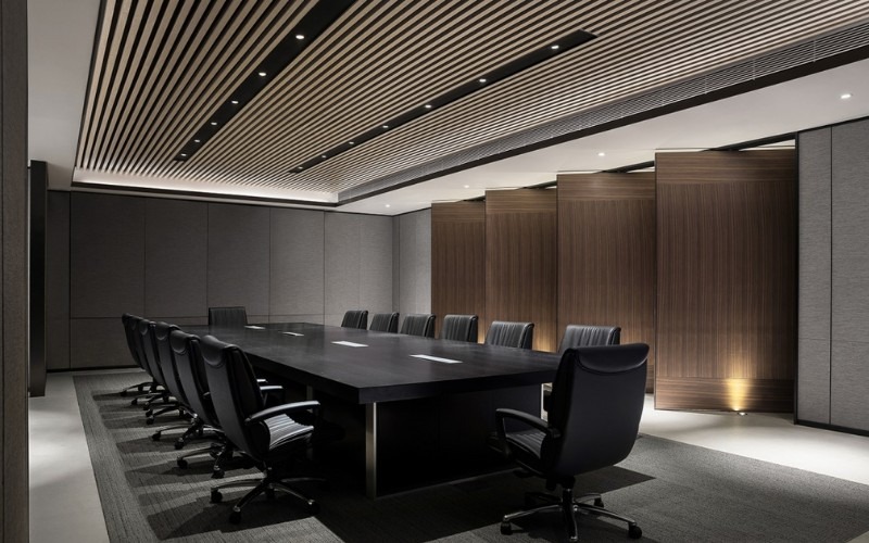 Phòng họp hiện đại với bàn dài và ghế xoay da đen, trần nhà ốp gỗ sang trọng và ánh sáng tinh tế.