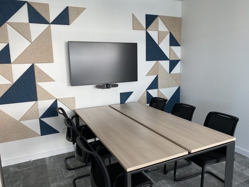 Phòng họp nhỏ gọn với bàn gỗ, ghế đen, tivi treo tường, trang trí họa tiết tam giác xanh be.