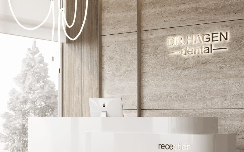 Quầy lễ tân tại phòng khám nha khoa sáng sủa với cây thông bên cửa sổ và máy tính trên bàn.