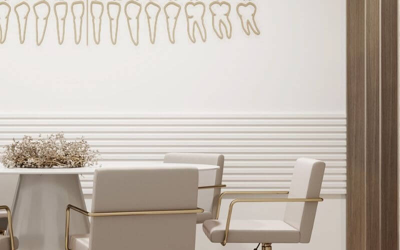 Phòng khám nha khoa hiện đại với tranh nghệ thuật răng treo tường, bàn ghế trắng sang trọng.
