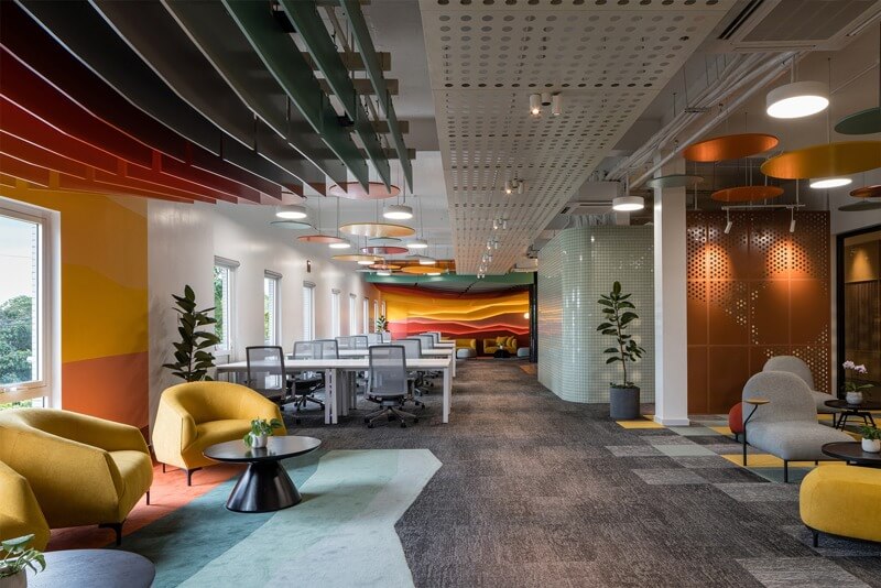 Không gian văn phòng hiện đại với trang trí sáng tạo, ghế màu vàng, bàn trắng, và cây xanh.