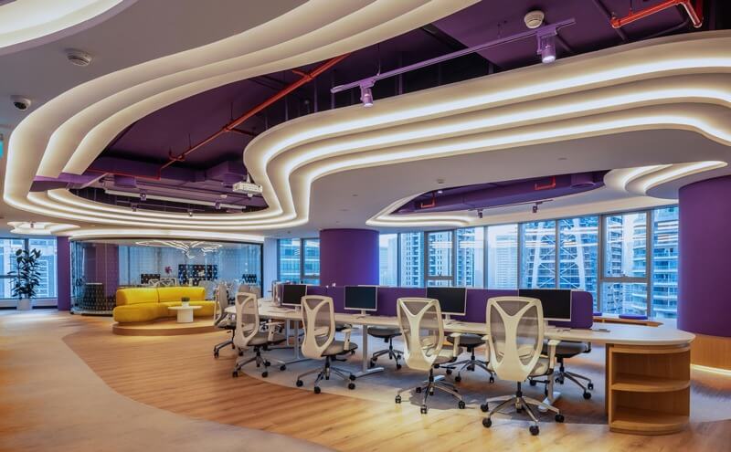 Văn phòng hiện đại với bàn ghế trắng, trần thiết kế độc đáo và ánh sáng tự nhiên từ cửa sổ lớn.