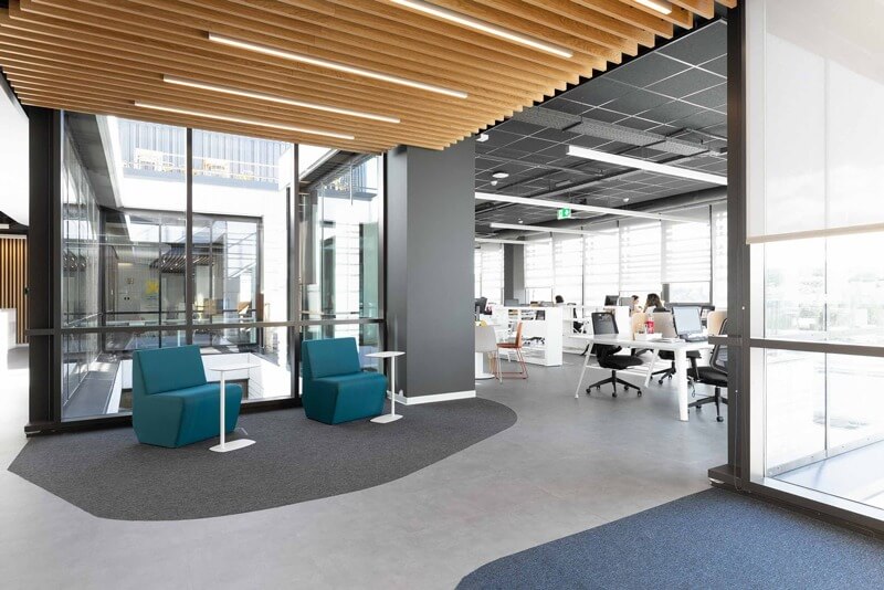 Khu vực làm việc mở với ghế xanh và bàn trắng, thiết kế hiện đại, ánh sáng tự nhiên qua cửa sổ lớn.