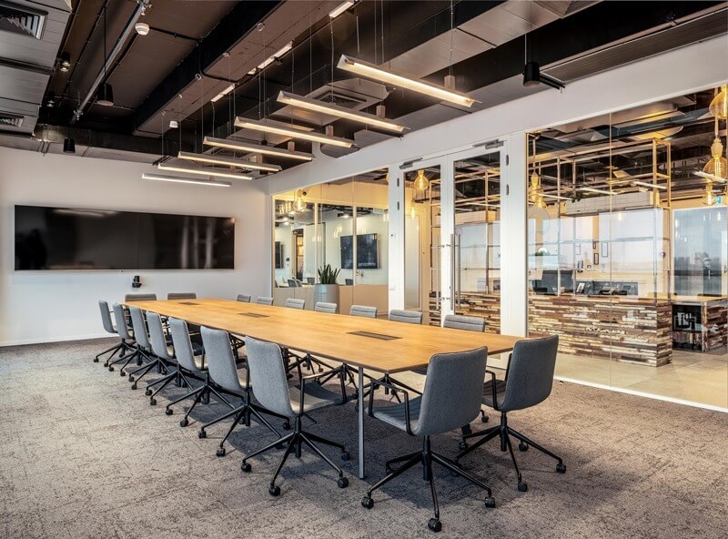 Phòng họp hiện đại với bàn dài và ghế xoay, ánh sáng đèn trần và tường kính trong suốt.