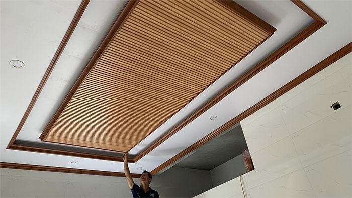 Người đàn ông cài đặt trần gỗ trang trí nội thất hiện đại trong một căn phòng.