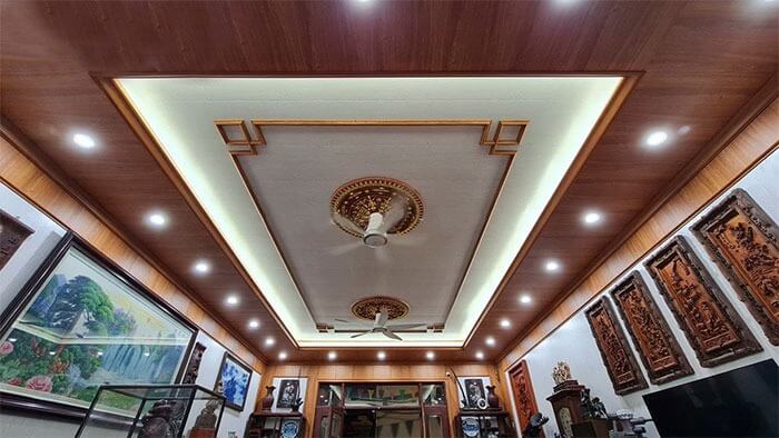 Trần nhà gỗ sang trọng với đèn LED và quạt trần, trang trí chi tiết nghệ thuật tại phòng khách.