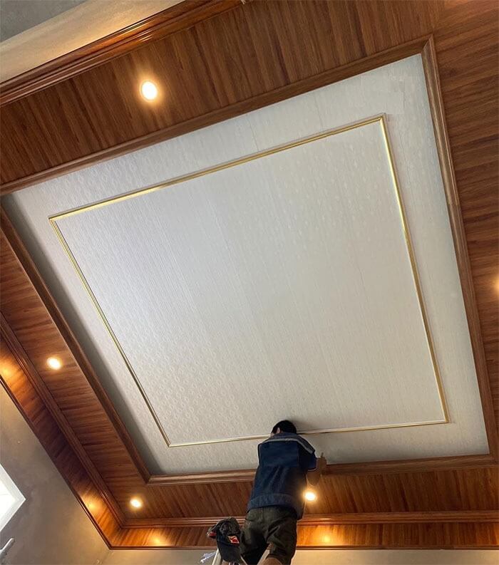 Công nhân lắp đặt trần thạch cao với viền gỗ và đèn chiếu sáng, tạo không gian nội thất sang trọng.