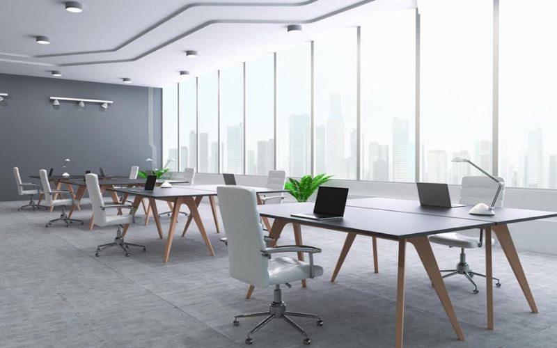 Văn phòng hiện đại với bàn ghế trắng, cửa sổ lớn, ánh sáng tự nhiên và cây xanh, tạo không gian làm việc thoải mái.