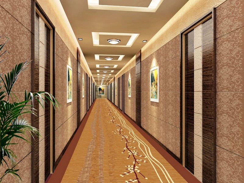 Hành lang khách sạn hiện đại với thảm trải hoa văn, đèn trần sáng, và cây xanh tạo không gian sang trọng.