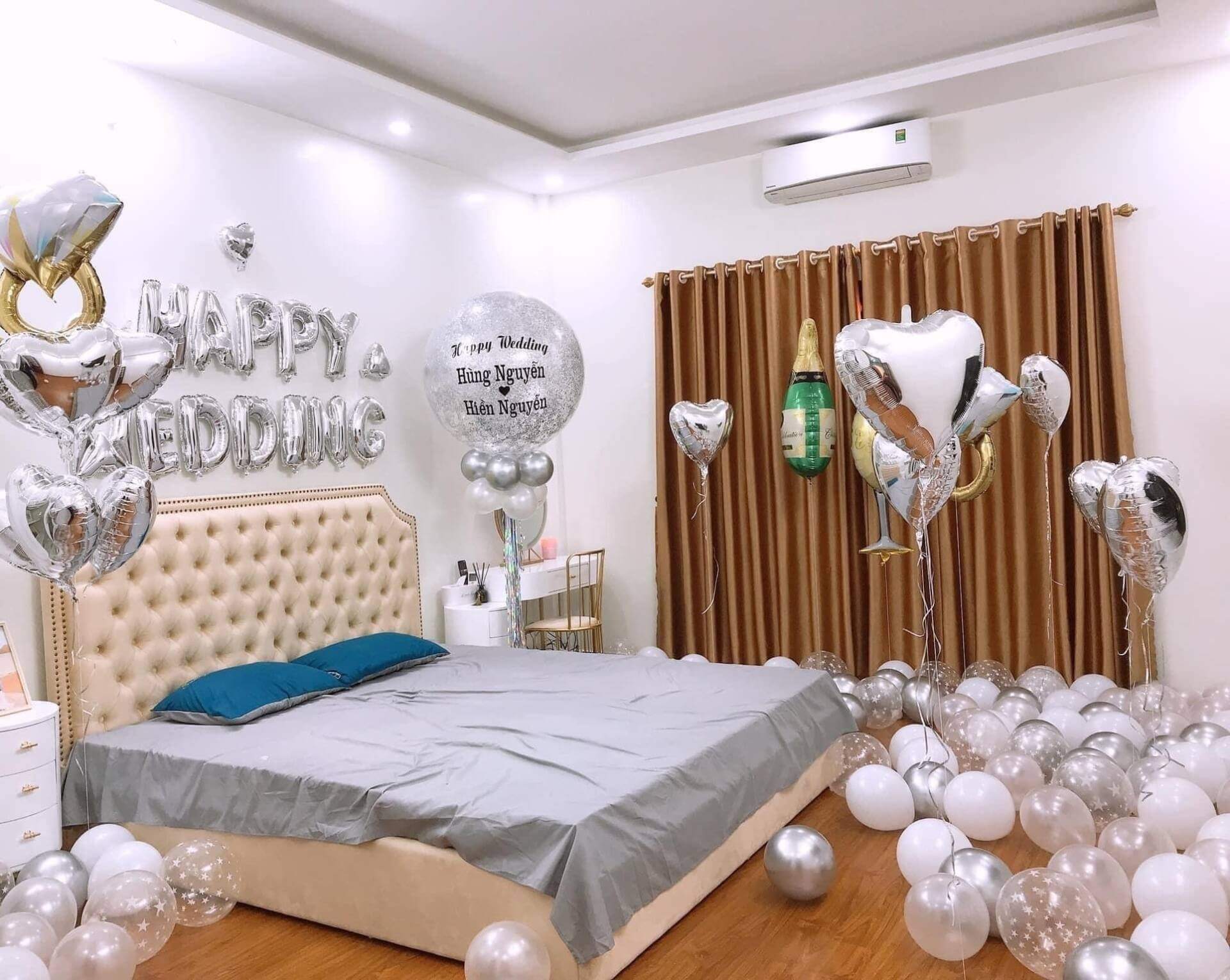 Phòng ngủ trang trí tiệc cưới với bóng bay và chữ Happy Wedding trên tường, tông màu trắng và bạc.