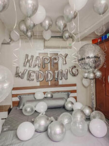 Trang trí phòng cưới với bóng bay màu bạc và chữ Happy Wedding trên giường.