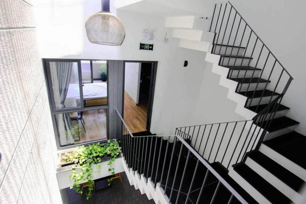 Cầu thang hiện đại với cây xanh, ánh sáng tự nhiên, và cửa sổ lớn kết nối với phòng ngủ, thiết kế tối giản.