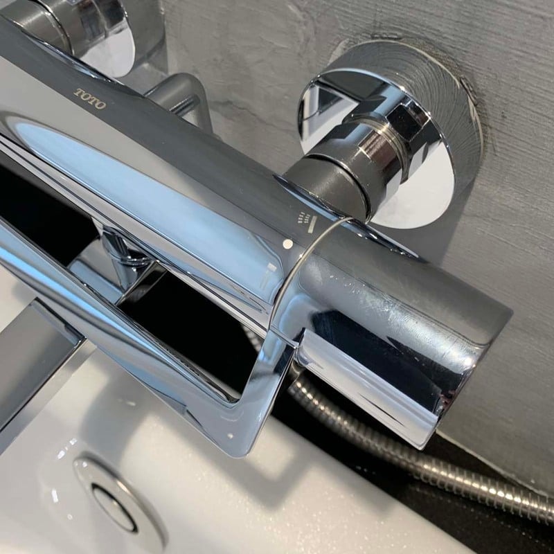 Vòi sen bằng thép không gỉ sáng bóng, gắn trên bồn tắm trắng trong phòng tắm hiện đại.