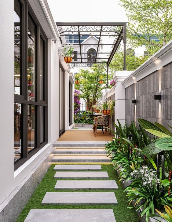 Lối đi ngoài trời với cây xanh, bàn ghế và giàn hoa trang trí, tạo không gian thư giãn thân thiện với thiên nhiên.