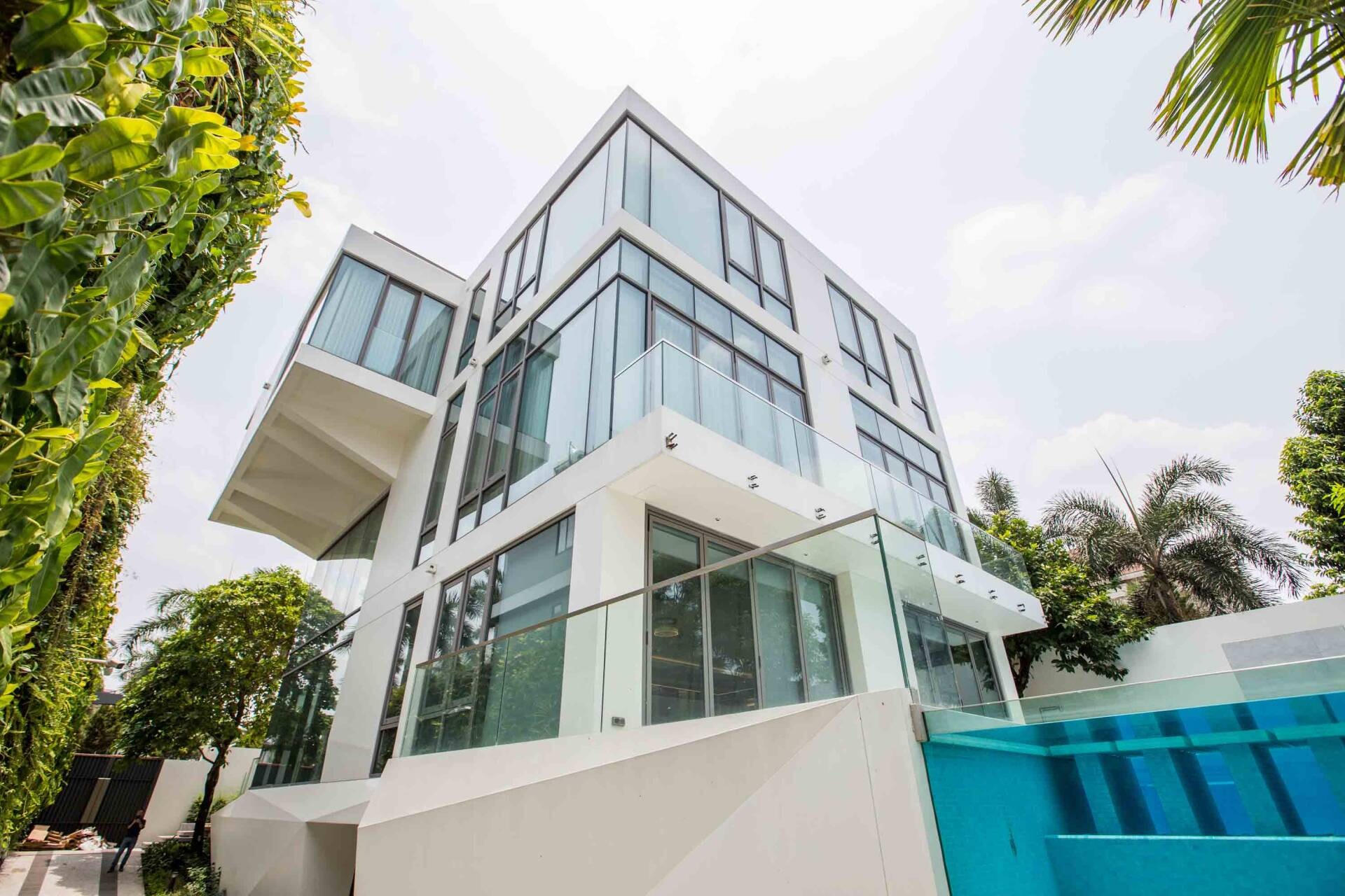 Biệt thự hiện đại với kiến trúc kính, hồ bơi xanh, xung quanh là cây xanh ở thành phố.