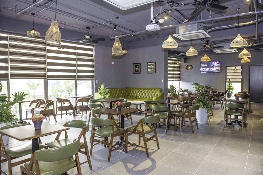 Quán cà phê hiện đại với đèn treo thả, nội thất gỗ và ghế sofa xanh, tạo không gian thoáng đãng, thư giãn.