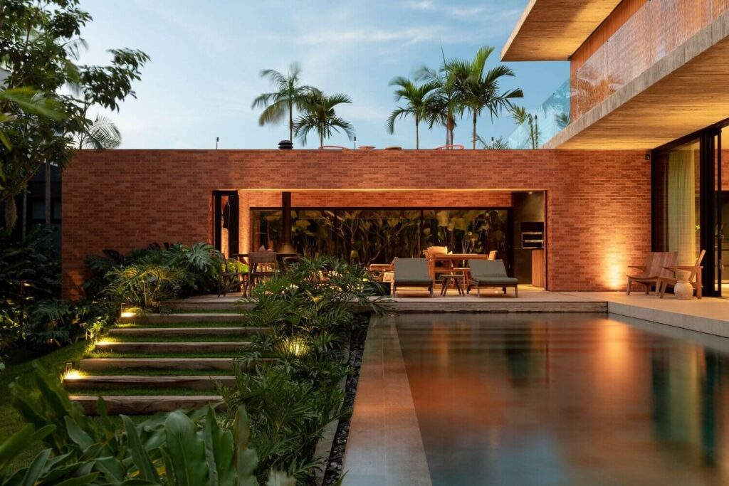 Biệt thự hiện đại với tường gạch đỏ, không gian ngoài trời sang trọng và hồ bơi, xung quanh cây xanh.