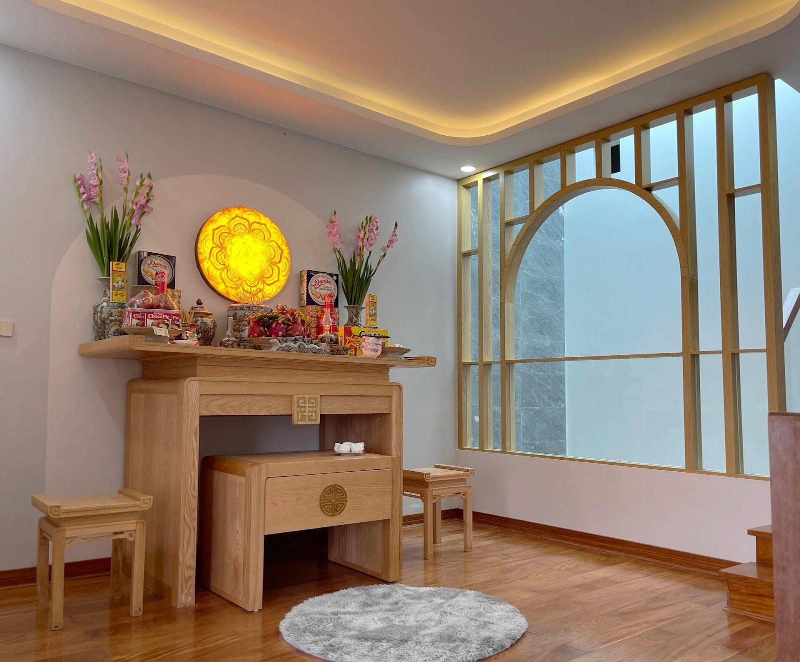 Gian thờ trong nhà với bàn thờ gỗ, hoa, nến và họa tiết truyền thống. Ánh sáng ấm cúng và trang trí tinh tế.