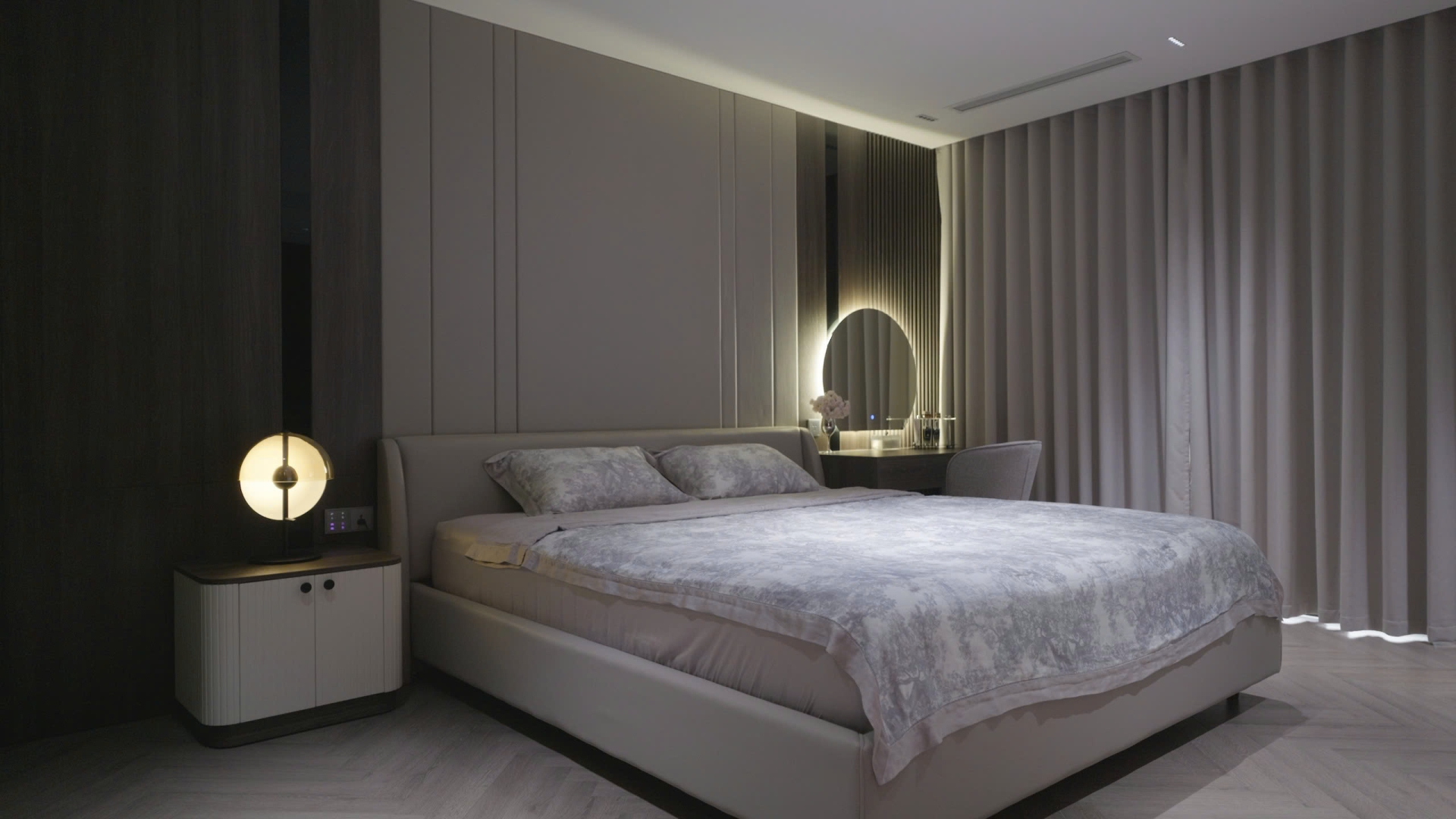 ngfiu7z2at9xlbj5ov8p Phòng ngủ hiện đại với giường đôi, đèn ngủ bật sáng, nội thất màu xám và bàn trang điểm bên cạnh.