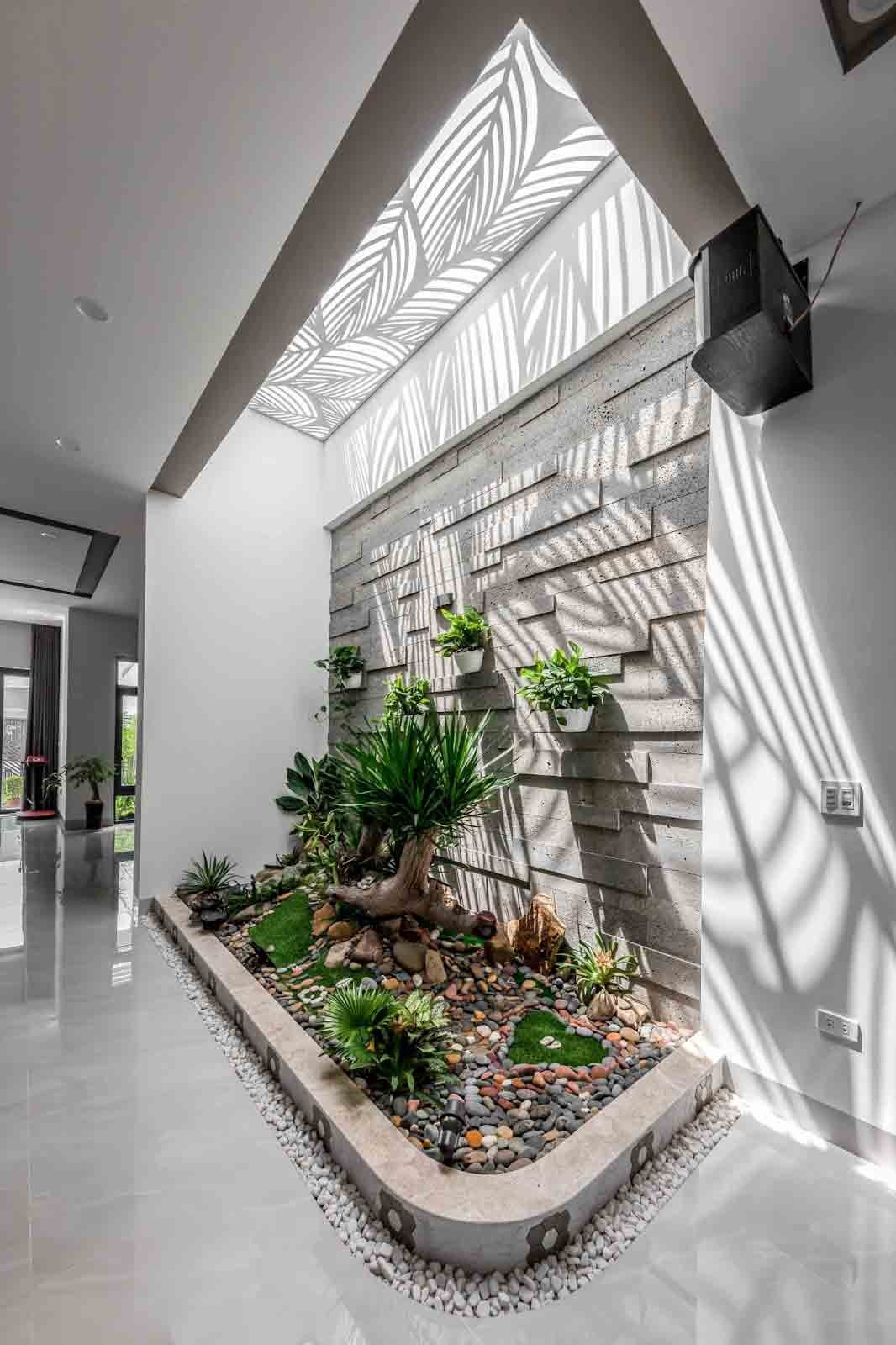 Không gian nội thất hiện đại với vườn cây xanh và ánh sáng tự nhiên chiếu qua mái, tạo họa tiết độc đáo.