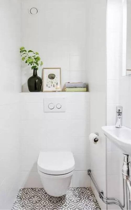 Nhà vệ sinh hiện đại với tường trắng, bồn cầu treo, chậu rửa nhỏ và cây xanh trang trí.