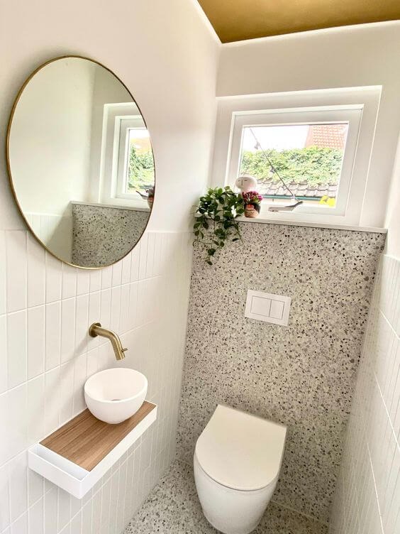 Phòng vệ sinh hiện đại với bồn rửa nhỏ gọn, gương tròn và cửa sổ cây xanh tạo không gian thoáng đãng.