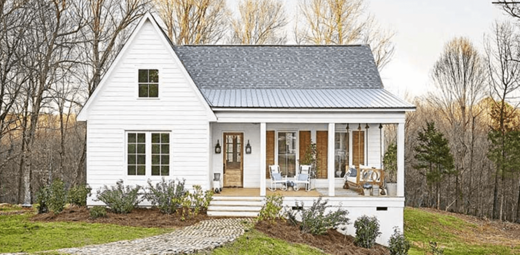 nha-2-mai-ton-3 Ngôi nhà cấp 4 màu trắng với mái hiên ở nông thôn, bao quanh bởi cây cối và không gian yên bình.