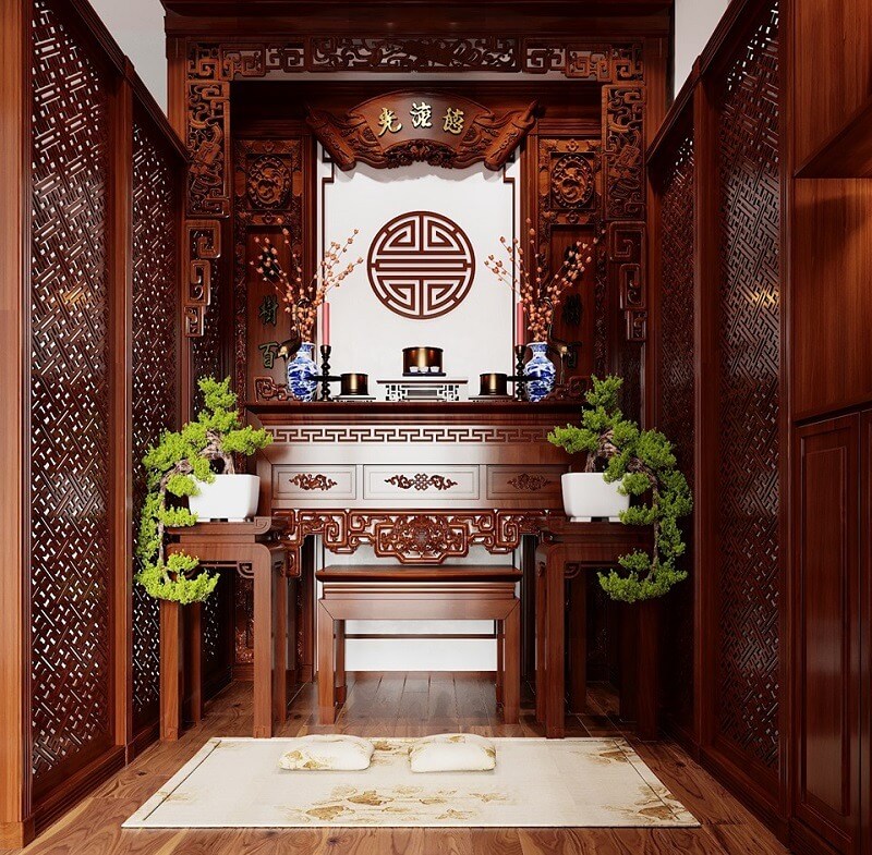 Bàn thờ gỗ chạm khắc tinh xảo, trang trí cây cảnh và bình hoa, mang phong cách truyền thống Việt Nam.