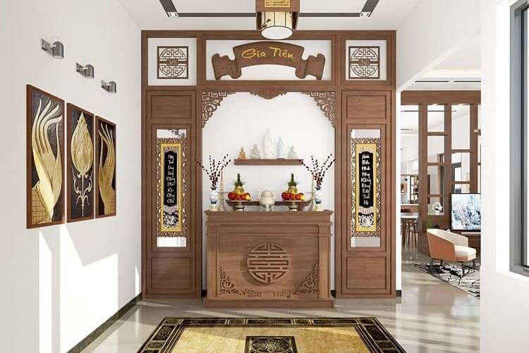 Bàn thờ gia tiên gỗ trang trí với hoa và trái cây, phòng thờ trang nghiêm, có tranh treo tường và ánh sáng tự nhiên.