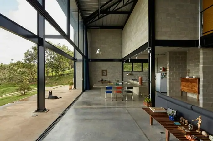 Nhà hiện đại khung thép, cửa kính lớn nhìn ra sân vườn xanh mát. Nội thất tối giản với bàn ghế đa màu sắc.