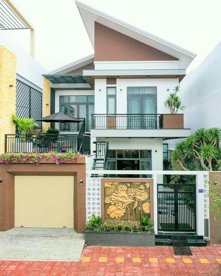 Nhà phố hai tầng hiện đại với mái chéo, ban công và cổng trước trang trí hoa văn tinh tế.