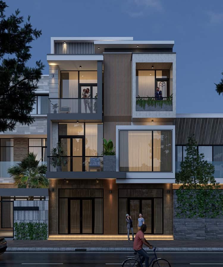 Nhà phố hiện đại ba tầng về đêm, có ban công cây xanh và người đi xe đạp phía trước.