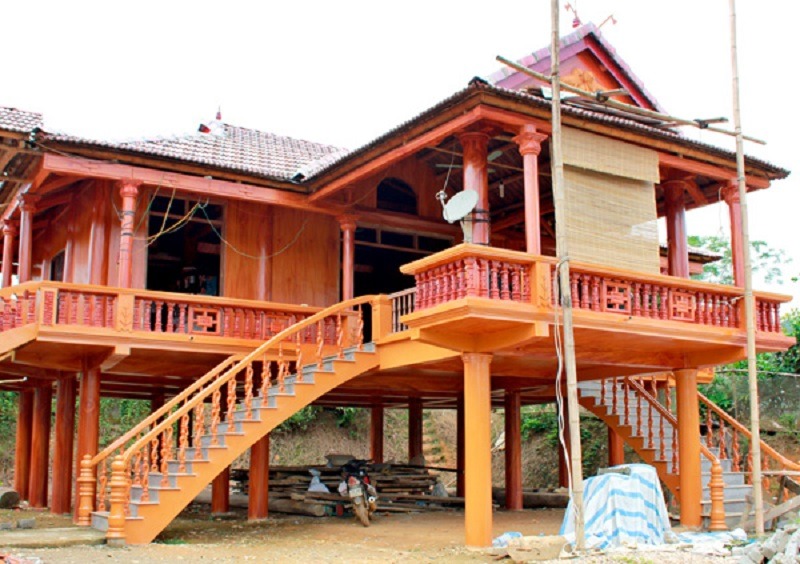 Nhà sàn gỗ truyền thống với mái ngói, cầu thang uốn lượn và bức rèm tre treo phía trước.