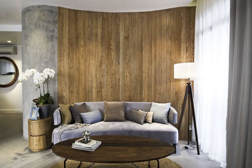 nhung-diem-noi-bat-cua-phong-cach-nhiet-doi4 Phòng khách hiện đại với ghế sofa xám, tường gỗ, đèn đứng, bàn tròn và bình hoa lan trắng.