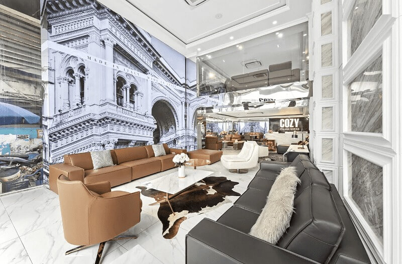 Phòng khách sang trọng với sofa da nâu, trang trí ảnh kiến trúc cổ điển, sàn lát gạch trắng, đèn trần hiện đại.