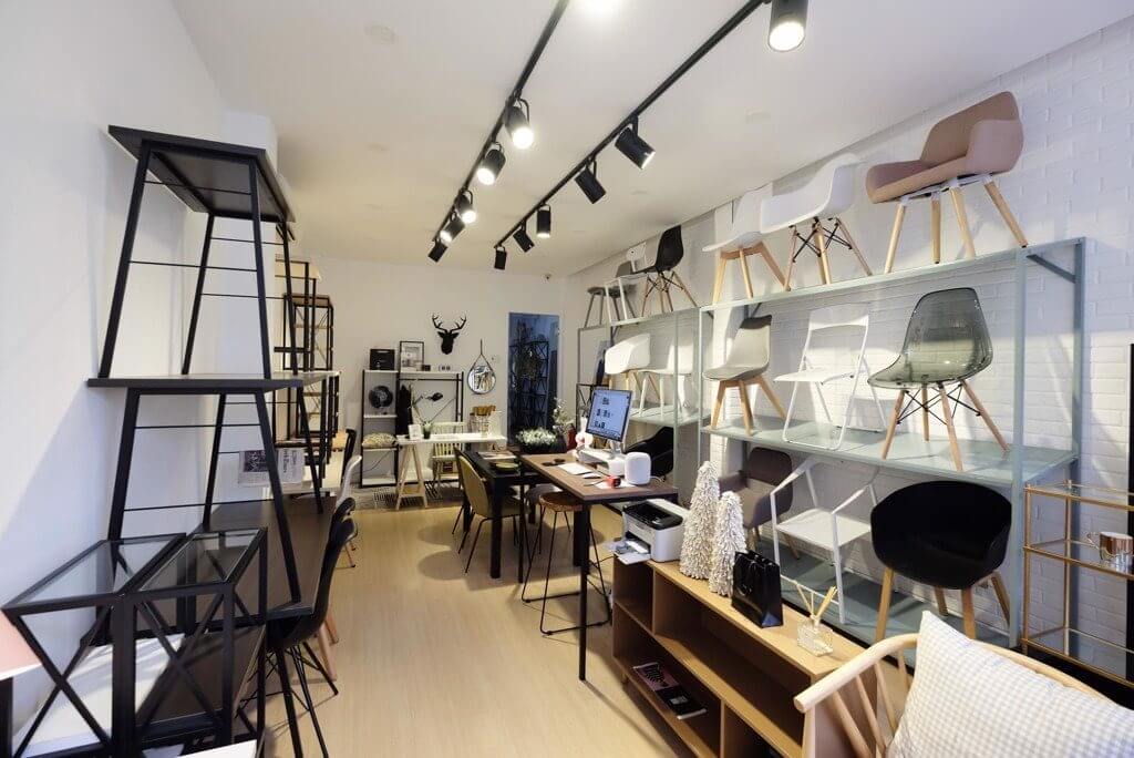 Cửa hàng nội thất hiện đại với nhiều mẫu ghế trưng bày trên kệ và bàn làm việc có máy tính.