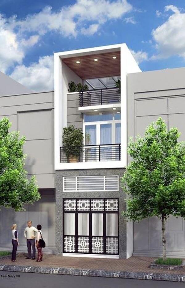 Nhà phố hiện đại với ban công và cây xanh phía trước dưới bầu trời xanh.