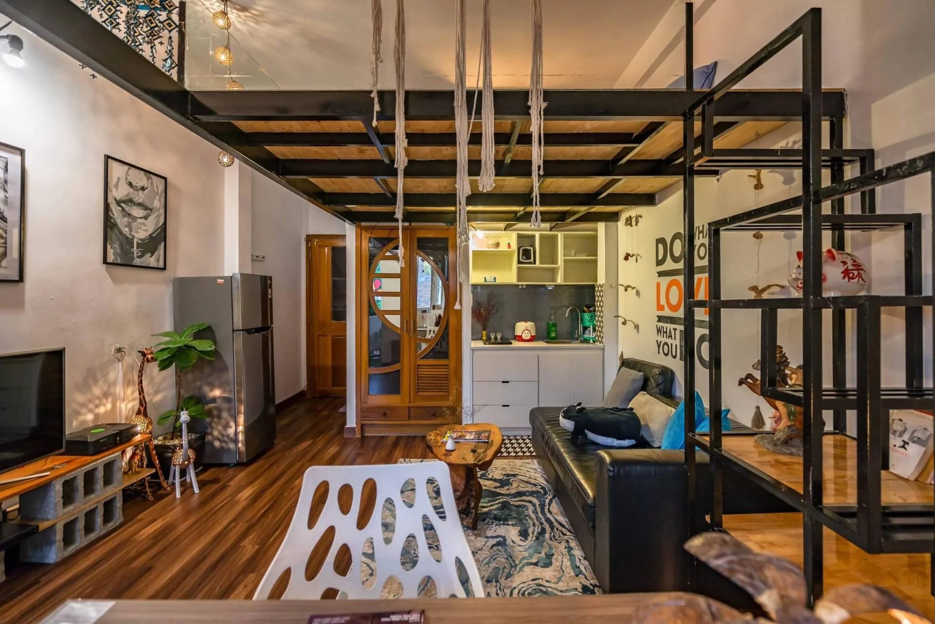 Phòng khách nội thất hiện đại với sofa da đen, bếp nhỏ, và kệ trang trí, ánh sáng ấm áp, phong cách tối giản.